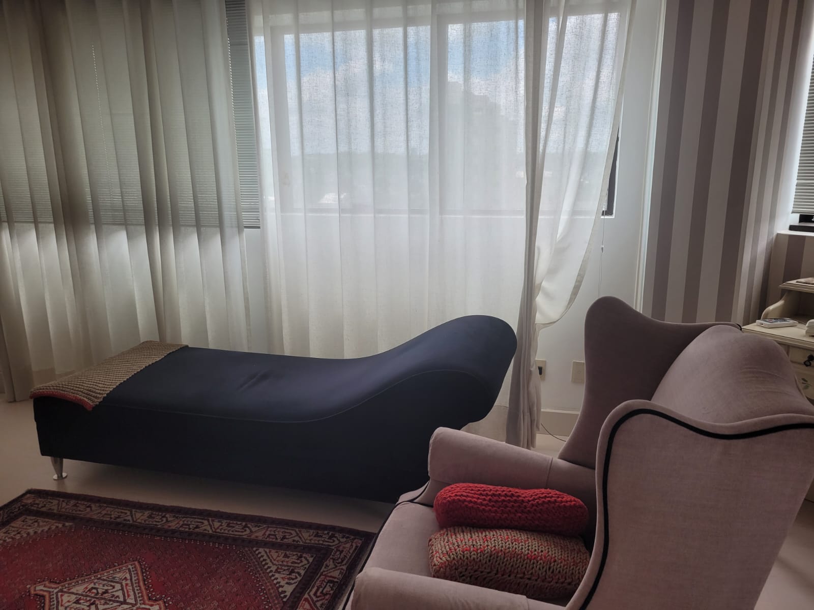 Sala de atendimento do consultório: divã, poltrona e janela com cortina clara